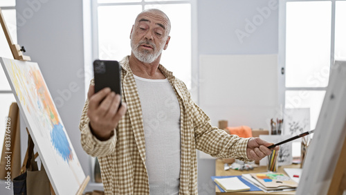 Foto Mature man with grey beard taking selfie in an art studio while painting on canvas, showcasing creativity and leisure