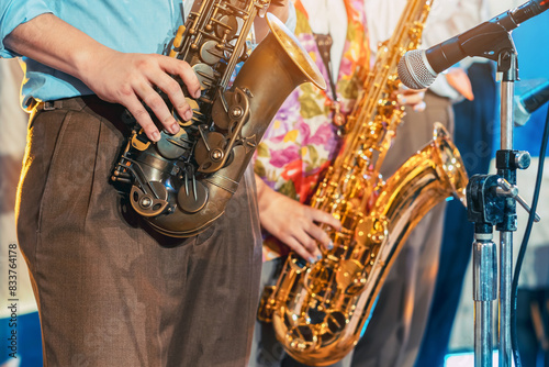 Musician playing saxophone on blurred background. Man with friends blow saxophone with the band for performance. Music instrument played by saxophonist player musician in festival. Selective focus.