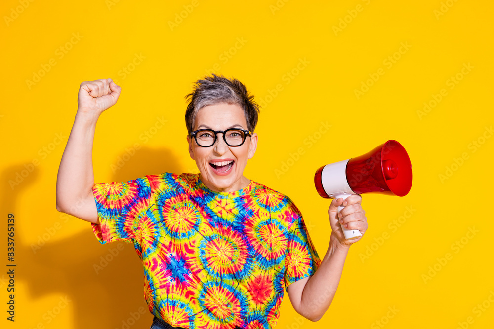 Portrait of nice aged lady raise fist loudspeaker wear t-shirt isolated on yellow color background Portrait of nice aged lady raise fist loudspeaker wear t-shirt isolated on yellow color background
