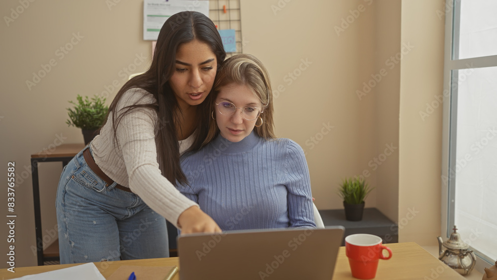 Two women collaborating on a project with a laptop in a modern home office setting. Two women collaborating on a project with a laptop in a modern home office setting.