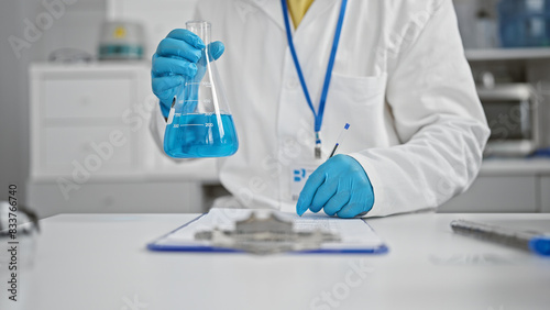 Scientist examining blue liquid in a flask with equipment in a white laboratory setting.