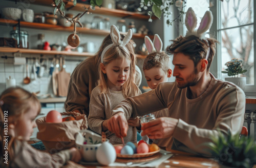 Family doing Easter crafts together  including children wearing bunny ears and painting eggs with red paint on the table in their kitchen