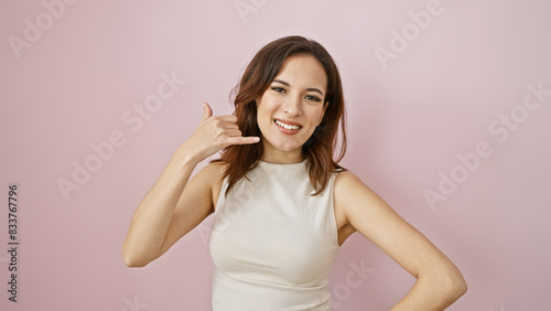 A smiling young hispanic woman gestures calling with her hand  against a soft pink isolated background.