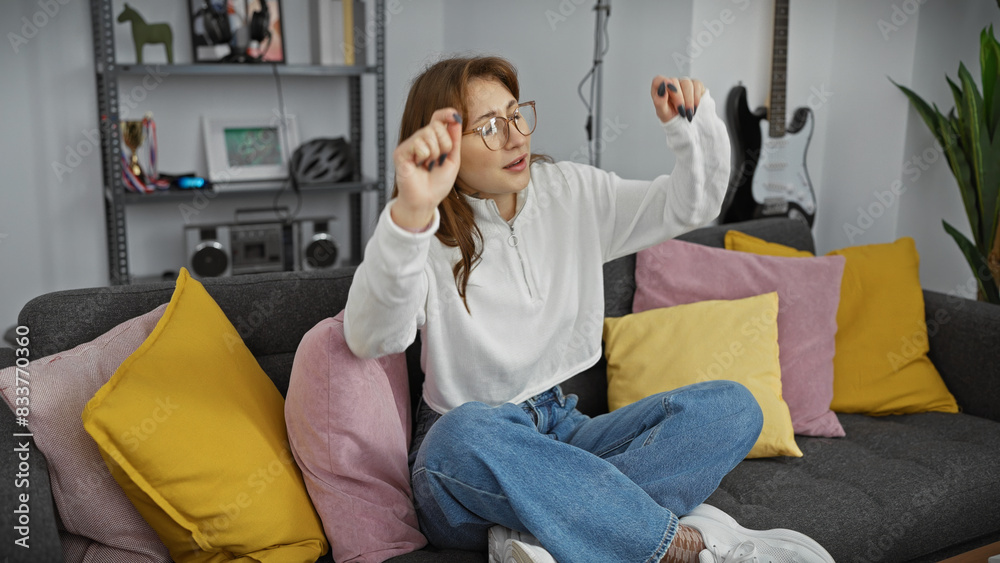 Obraz premium A young caucasian woman dances joyfully in a cozy living room setting, embodying leisure and relaxation at home.