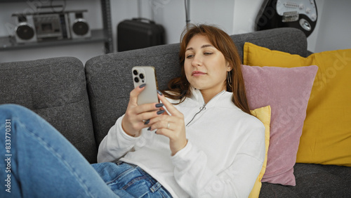 Photos A relaxed young woman lounges on a couch using her smartphone in a cozy living room setting