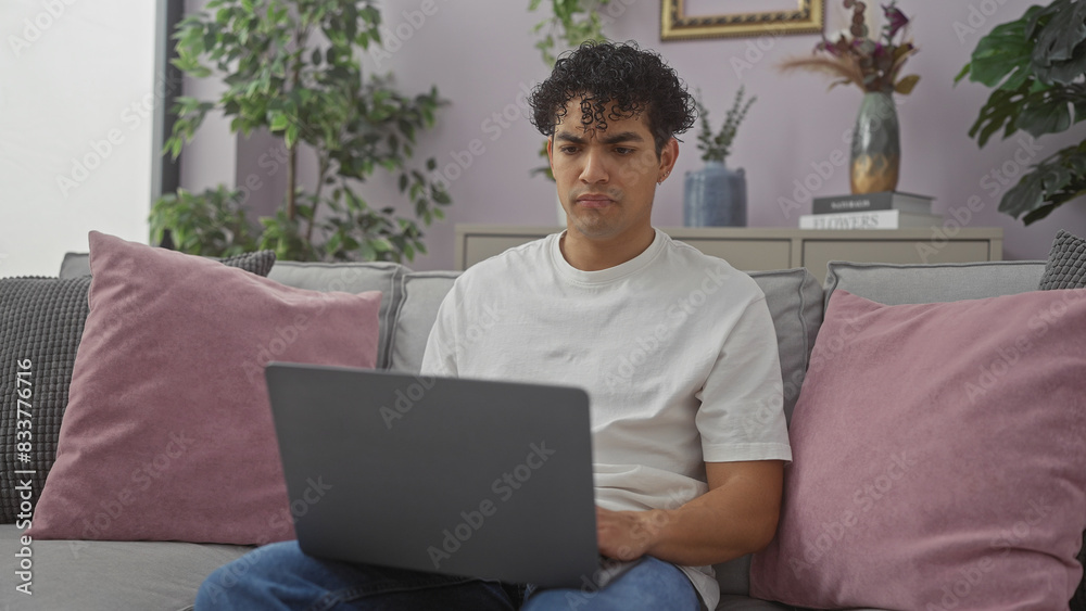 Young hispanic man using laptop on sofa in cozy living room interior Young hispanic man using laptop on sofa in cozy living room interior