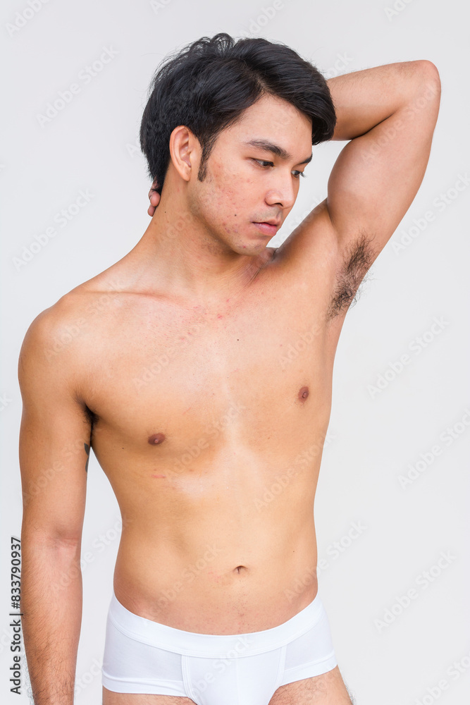 A handsome Asian man in white briefs posing confidently with his arm raised. Ideal for fashion, lifestyle, and fitness concepts. A handsome Asian man in white briefs posing confidently with his arm raised. Ideal for fashion, lifestyle, and fitness concepts.