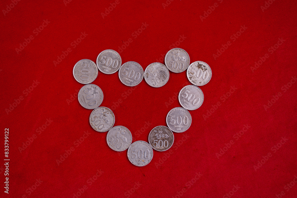 A collection of 500 rupiah coins forming a love isolated on a bright red background A collection of 500 rupiah coins forming a love isolated on a bright red background