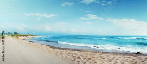 Fototapeta Naklejka Na Ścianę i Meble -  An empty asphalt road with copy space image borders a serene beach under a clear blue sky.