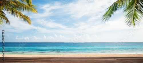 Ideal vacation scenery of a summer tropical ocean with waves  palm fronds  a blue sky with clouds  and an empty wooden table providing a copy space image.