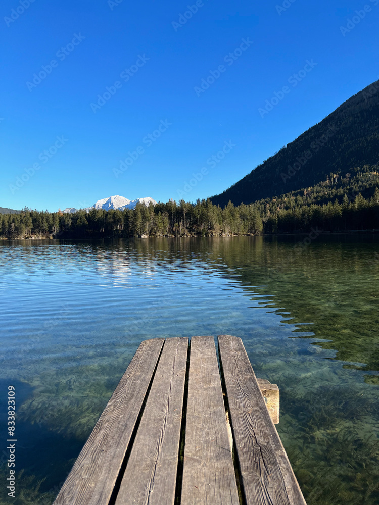 Small wooden pier on the clear waters of Lake Hintersee in Bavaria, Germany, with forested shoreline and mountain backdrop. Small wooden pier on the clear waters of Lake Hintersee in Bavaria, Germany, with forested shoreline and mountain backdrop.