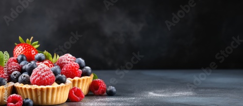 Tasty tartlets topped with raspberries and blueberries on a slate backdrop, ideal for a copy space image.