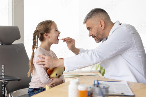 Attentive doctor. Determined professional male doctor examining little girl patient and looking in her throat during checkup