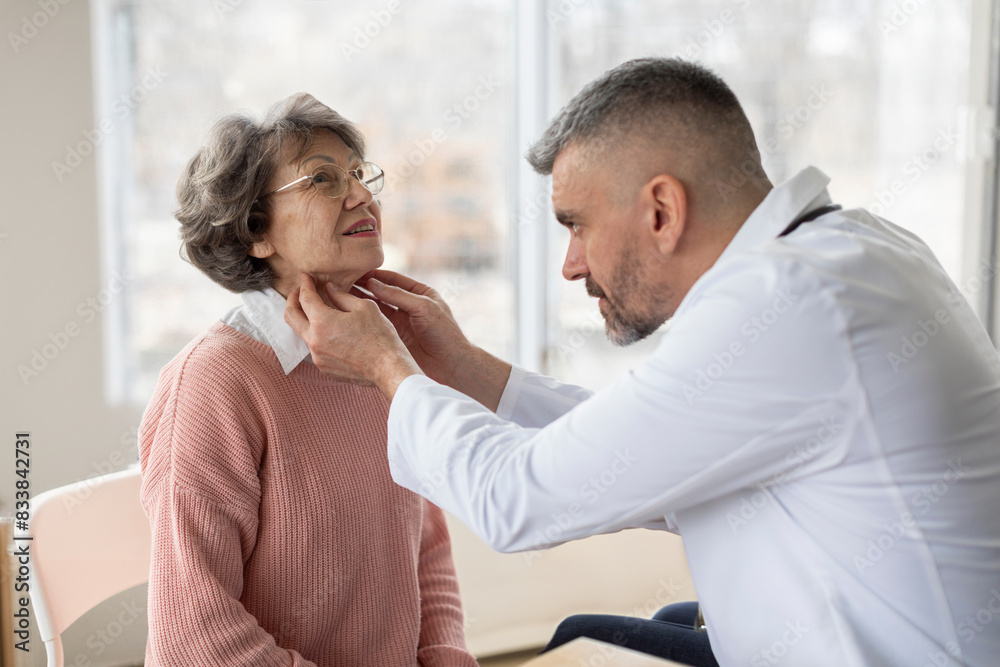 Professional male doctor palpating neck of senior female patient while examining her during consultation in private clinic office Professional male doctor palpating neck of senior female patient while examining her during consultation in private clinic office