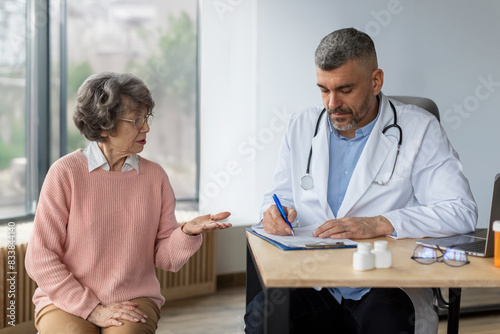 Senior woman on check up appointment with her doctor writing symptoms in flipboard and listening her. Checkup, prevention examination, diagnosis, medicine concept photo