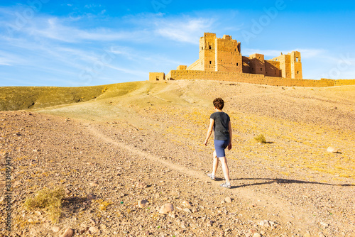 Young woman tourist walking to Tamnougalt kasbah castle in Atlas Mountains, Morocco, North Africa