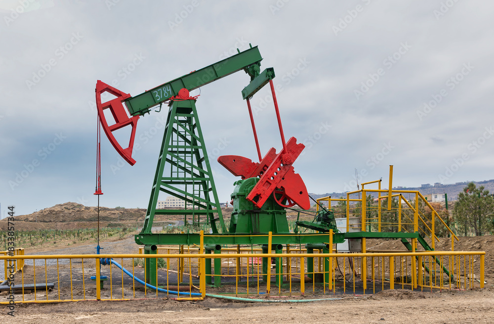 An operational green and red oil pumpjack surrounded by yellow fencing, set against a cloudy sky, in Baku, Azerbaijan An operational green and red oil pumpjack surrounded by yellow fencing, set against a cloudy sky, in Baku, Azerbaijan