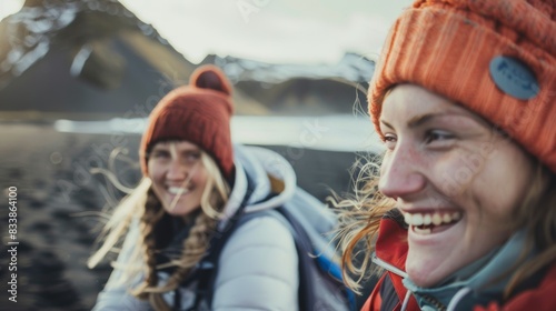 Two women in winter gear smiling with snow-capped mountains in the background enjoying a hike or outdoor adventure.