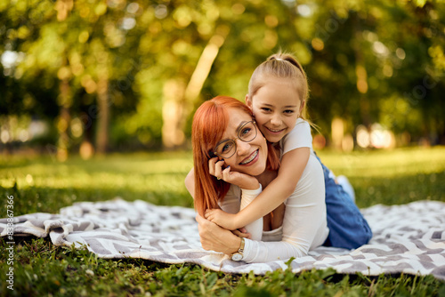 Portrait of a lovely mother lying on a blanket outdoors and her daughter lying on her back, smiling for the camera. photo