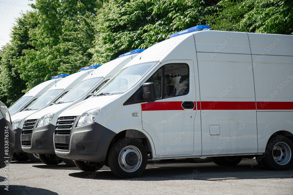Multiple new white ambulance vans parked near a hospital