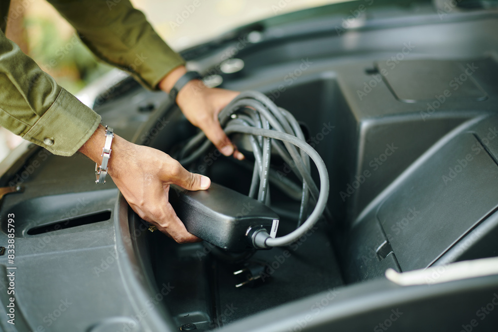 Hands of owner putting charging cable in trunk of hybrid car