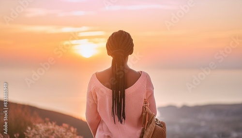 Black woman looking at the sunset; back view; body of water and mountains 