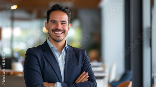 Smiling elegant confident young professional Latino Hispanic businessman, showcasing leadership and sophistication, standing in a spacious office photo