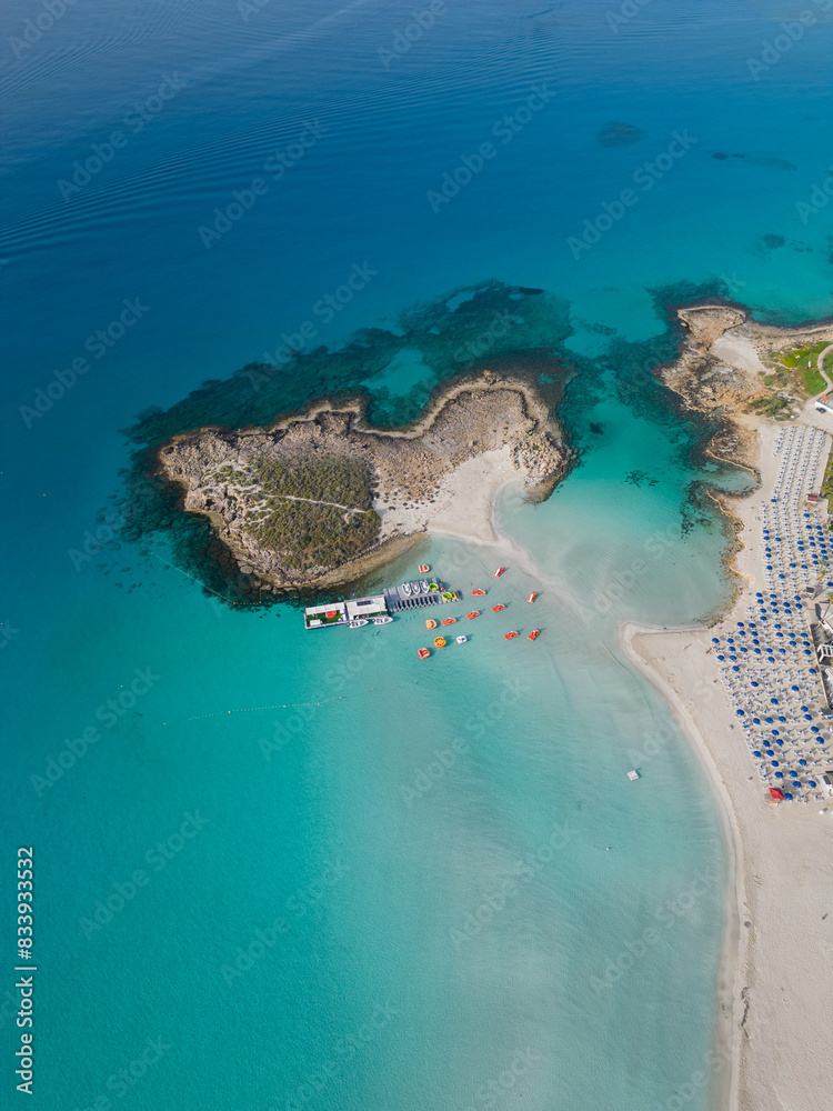 Nissi beach with Nissi island in the morning. High altitude aerial vertical view. Calm sea on a sunny morning with no people in Ayia Napa, Cyprus. Turquoise and deep blue Mediterranean sea.