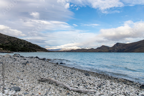 Low angle view along pebblestone beach with dead branches and water of Lago Grey lake in Torres del Paine National Park, Patagonia, Chile with snowcapped mountains in background photo