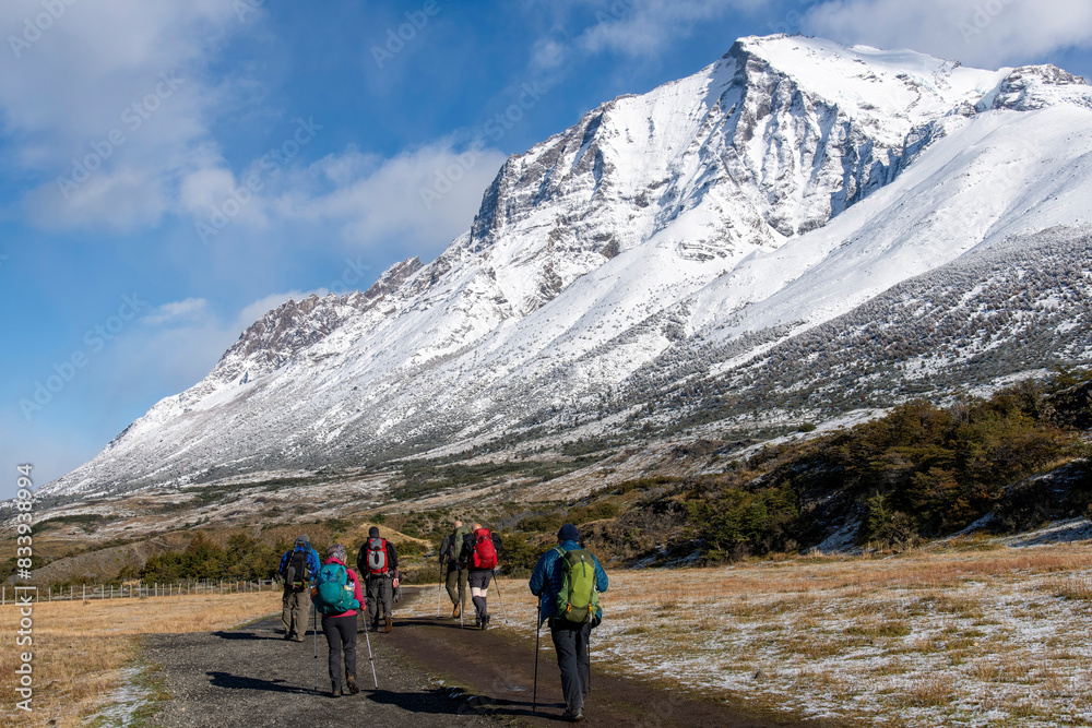 Fototapeta premium Torres del Paine National Park, Patagonia, Chile; hikers walking towards the lookout point for the three iconic granite towers (torres) on the W-trek route surrounded by snow covered mountains