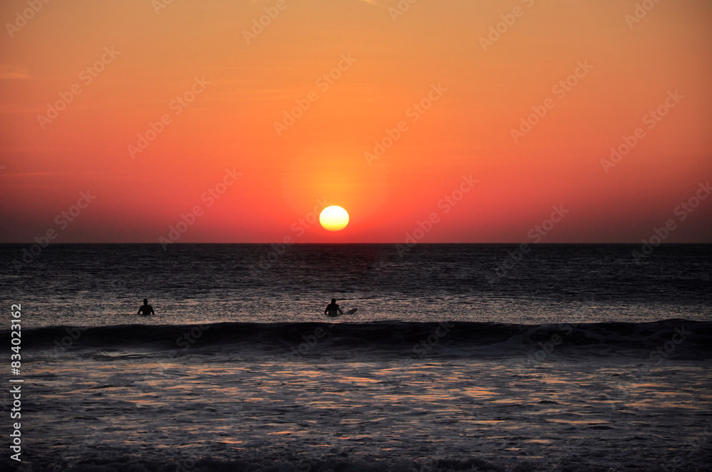 Paisaje marino horizontal con puesta de sol anaranjada y surfistas en el agua en una playa de Costa Rica. Paisaje marino horizontal con puesta de sol anaranjada y surfistas en el agua en una playa de Costa Rica.