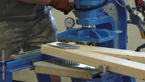 Balvi, Latvia - May 25, 2024 - Machine pressing metal plates into wooden beams, demonstrating an industrial joinery process in a workshop. photo