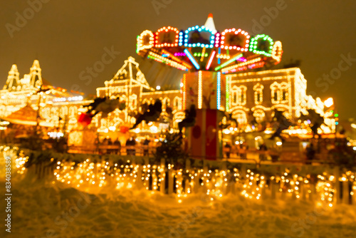 Defocused photo of people riding colorful carousel on Christmas Fair in winter with lots of lights and bokeh on snowy evening
