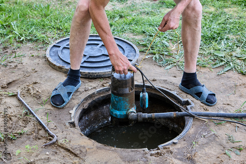 Septic tank maintenance, worker uses submersible waste water pump to pumping sewage out of tank. photo