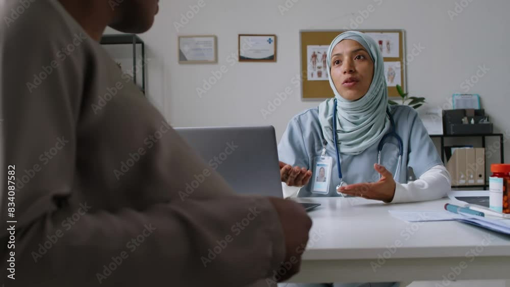 Medium shot of smiling young female obstetrician in Islamic hijab sitting at desk in clinic, consulting pregnant black woman stroking baby belly, giving advice and recommendations to prepare for birth Medium shot of smiling young female obstetrician in Islamic hijab sitting at desk in clinic, consulting pregnant black woman stroking baby belly, giving advice and recommendations to prepare for birth