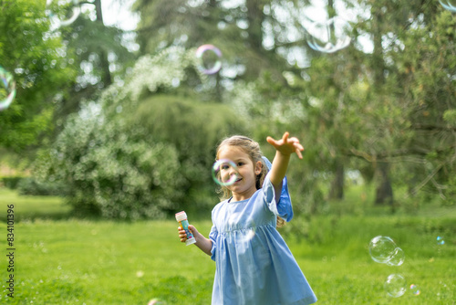 Joyful girl catching bubbles in a sunlit park, full of glee.