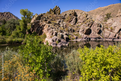 Cache la Poudre canyon in Fort Collins, CO.  Huge rock bluff, blue sky and trees.  Rocky background.  Scenic area with blue sky, tall mountain, tan bushes and trees. Gateway Natural Area.