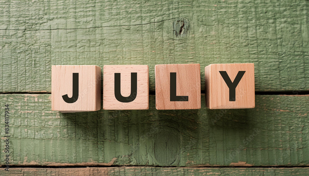 Fototapeta premium Wooden blocks with word JULY on green wood background. Summer time. Flat lay. Close-up.