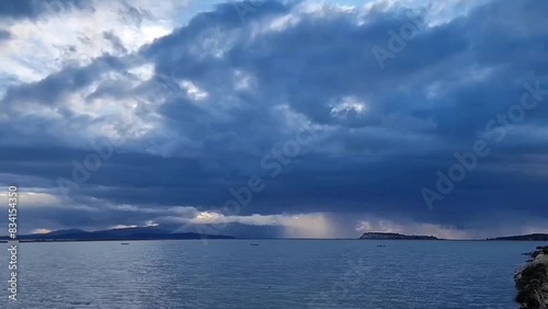 Black and grey clouds moving on a sea.  Sunlight is shining among the clouds.