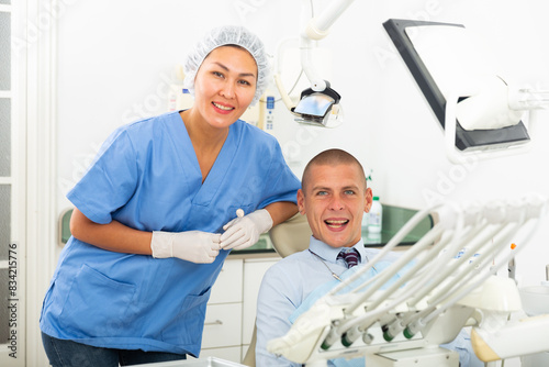 Portrait of a qualified asian woman dentist with a smiling man patient sitting in a dental chair at the clinic