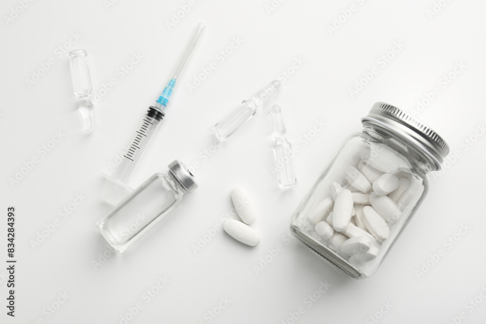 Glass ampoules with liquid, pills and syringe on white background, flat lay Glass ampoules with liquid, pills and syringe on white background, flat lay