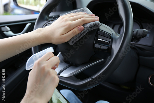 Woman cleaning steering wheel with rag in car, closeup