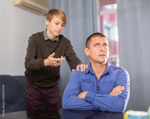 Upset adult man ignoring his son, teenage boy trying conversate with boy photo