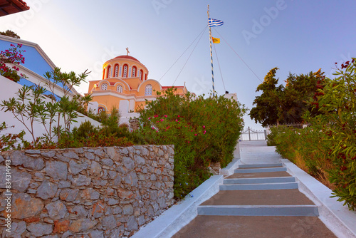 Panoramic view of The Annunciation Church with steps and Greek flag in Symi, Greece, at sunset photo