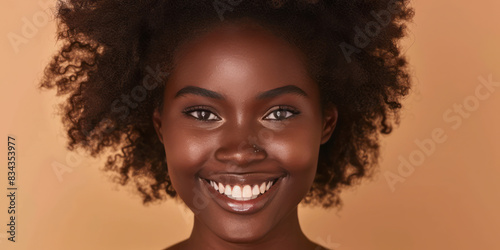 A model with beautiful afro hair is smiling against a beige background, her skin tone natural. © Duka Mer