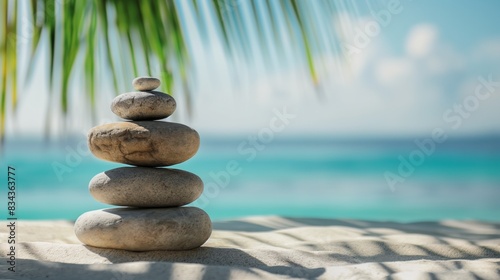 Stacked stones on white sandy beach under palm tree on sunny day.