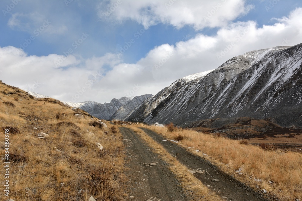 A field road climbs a grassy hill after rain to meet snow-covered mountain ranges.
