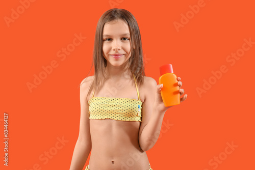 Cute little girl in swimsuit with glass of juice on orange background