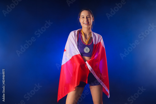 Sporty young woman with first place medal and flag of Canada on dark background photo
