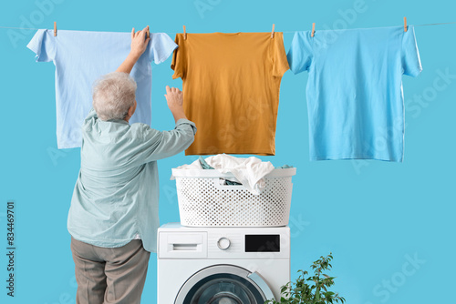 Senior woman doing laundry and hanging clothes on line on blue background